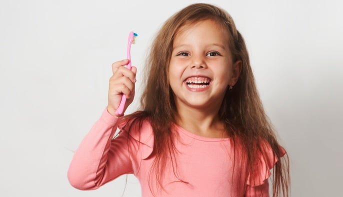 Little child girl brushing her teeth on white background.